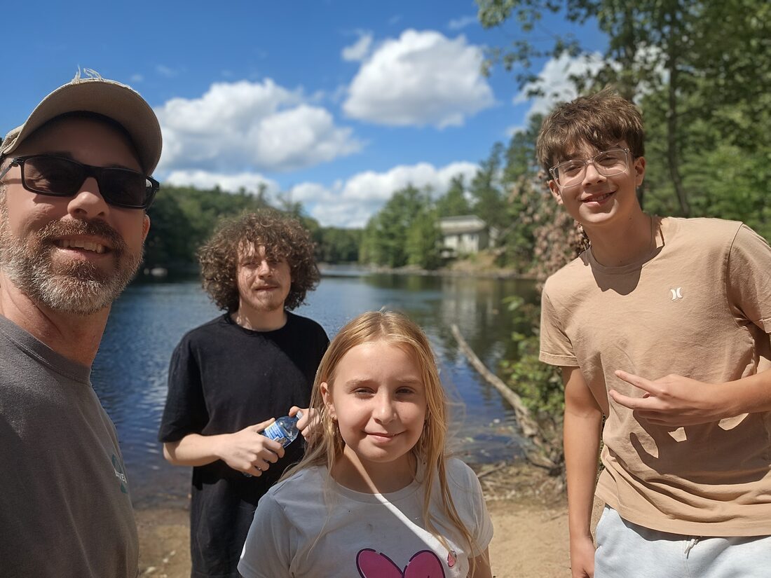 Kyle with his three kids, Mae, Max, and Cole, by a lake